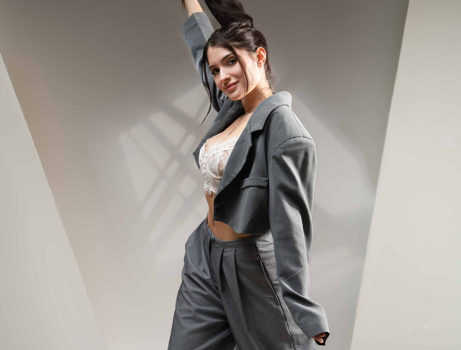 A person wearing a gray hoodie and black pants poses in different angles against a white wall.