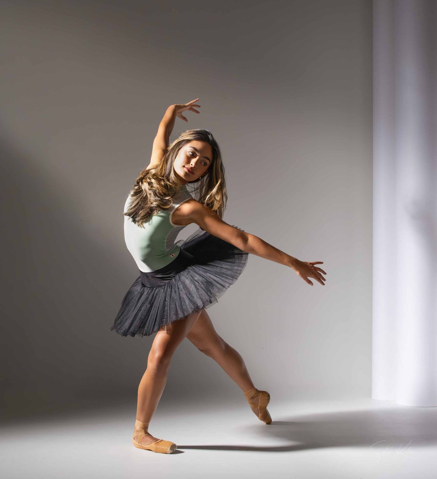 Graceful dancer in grey tutu performs expressive contemporary dance sequence in minimalist white studio space.
