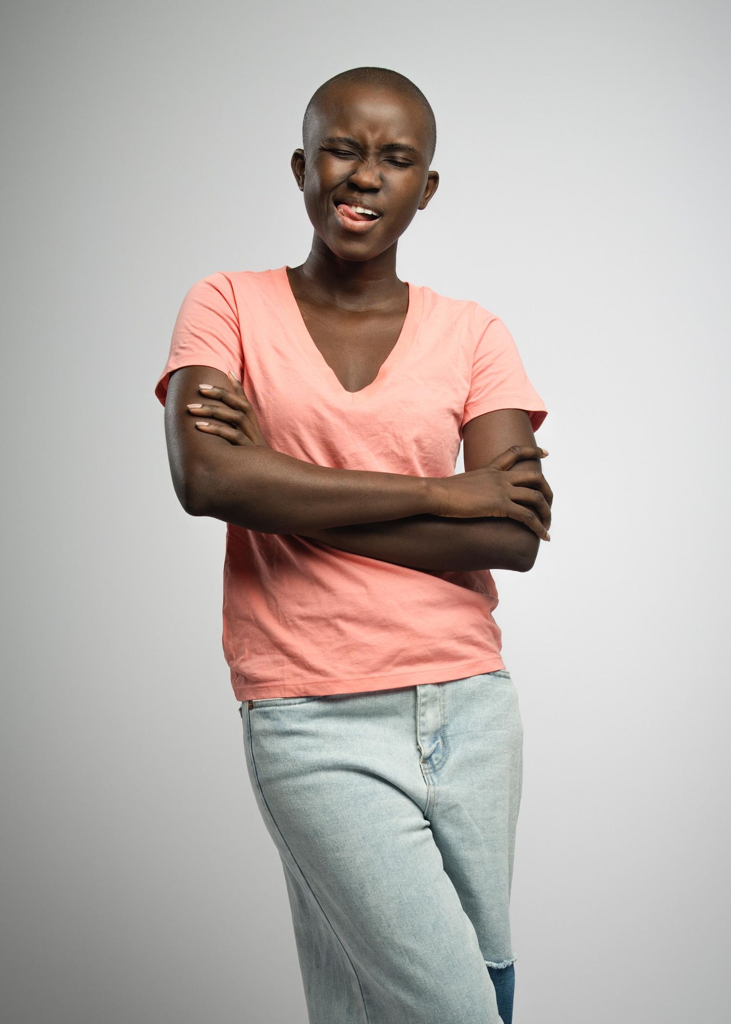 Figure in a peach-colored v-neck t-shirt and light jeans stands with arms crossed against a gray background.
