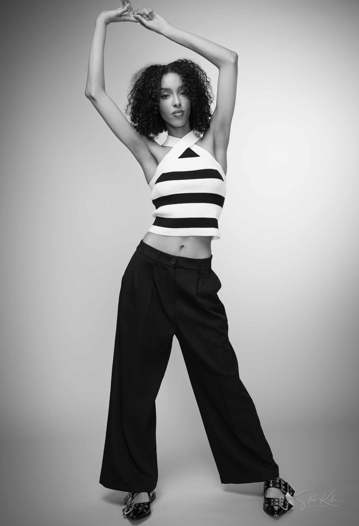 Fashion model in black and white striped crop top and wide-leg pants poses dynamically in monochrome studio series.