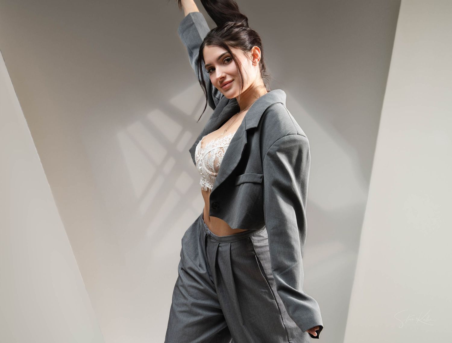 Model wearing a grey oversized blazer and matching pants with a white crop top in a minimalist setting.