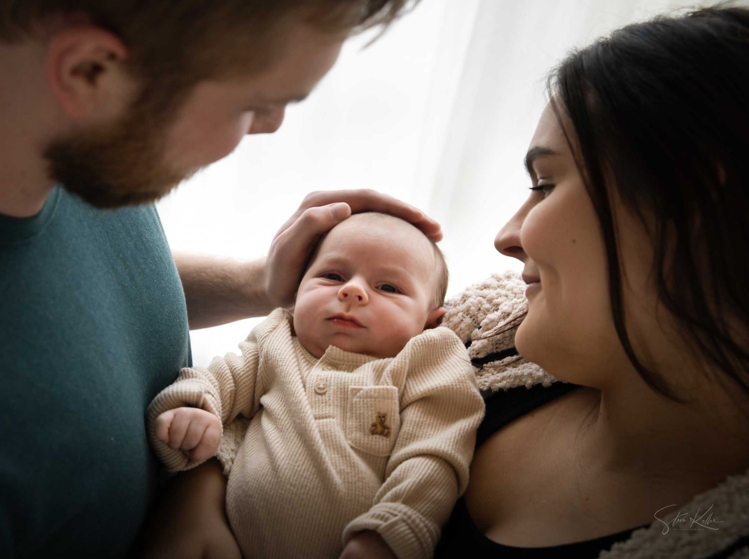 New parents lovingly gaze at their newborn baby, with father gently touching the infant's head.
