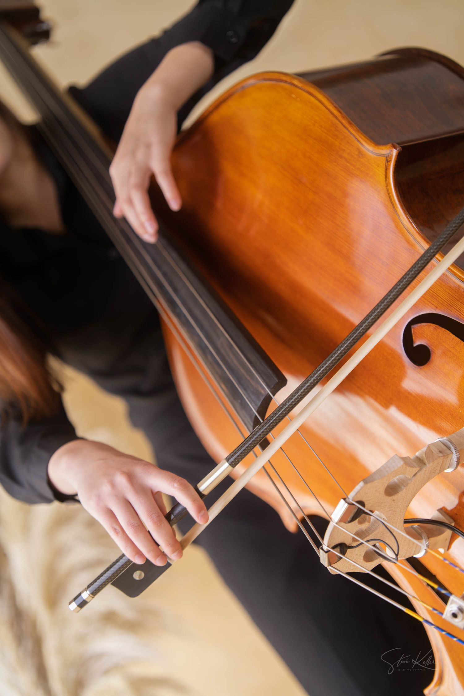 Close-up shot of hands playing a wooden cello with bow against warm honey-colored instrument body.