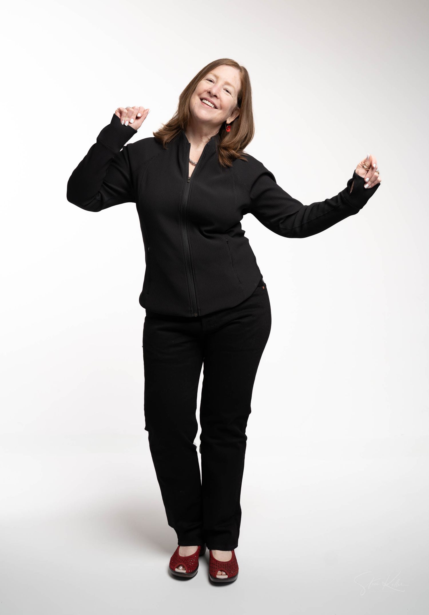 A person in a black business suit strikes a joyful pose with raised arms against a white background.