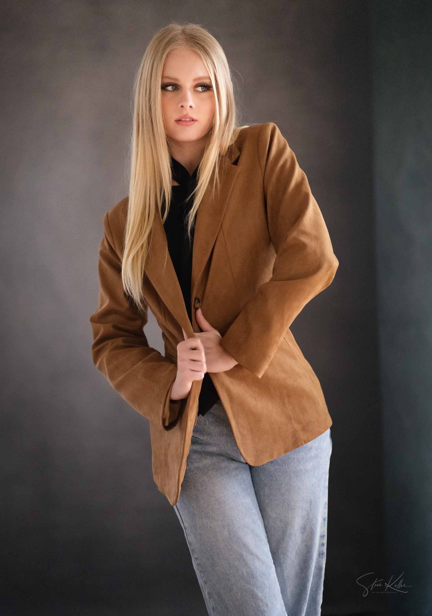 Fashion model in brown suede blazer and gray pants poses against dark studio backdrop in multiple poses.