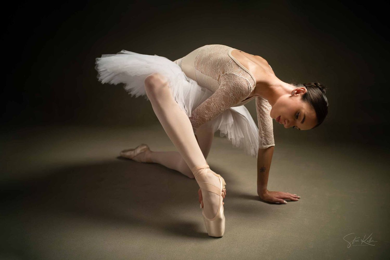 Ballet dancer in flowing pink tulle dress performs graceful movements in dramatic lighting against dark background.