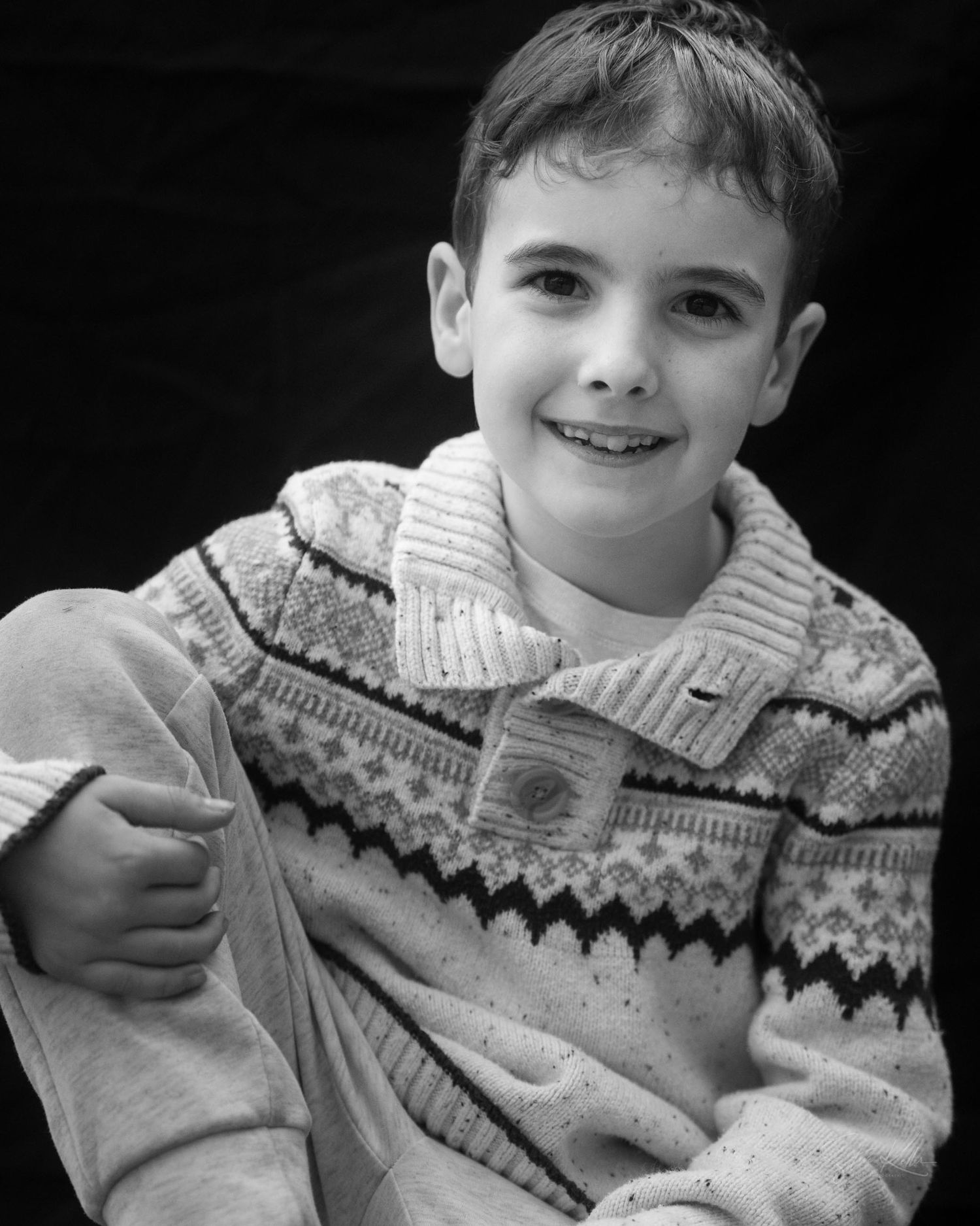 Black and white portrait of a young person wearing a patterned winter sweater with a cheerful expression.