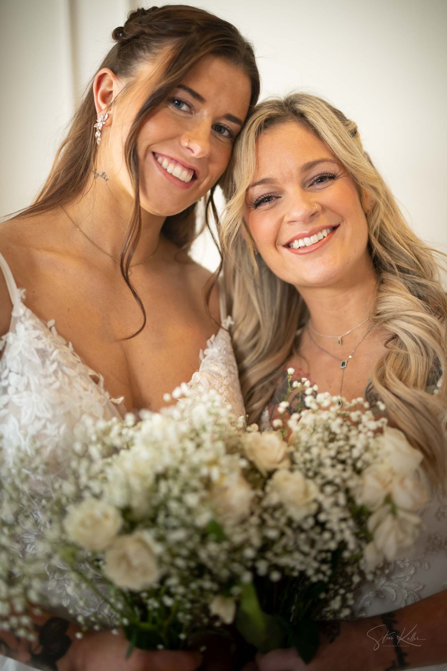 Two people in white wedding attire smile together while holding a bouquet of white roses and baby's breath flowers.