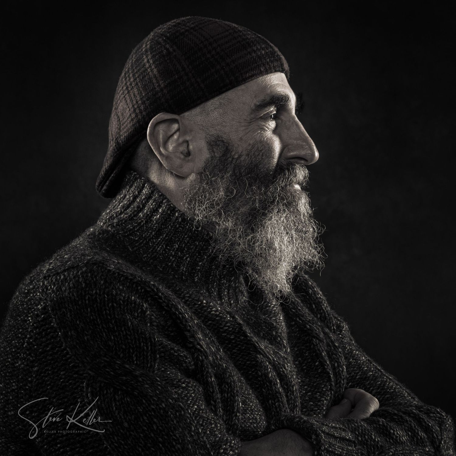 Black and white portrait of a bearded middle-aged man wearing a knit cap and turtleneck sweater, looking sideways.