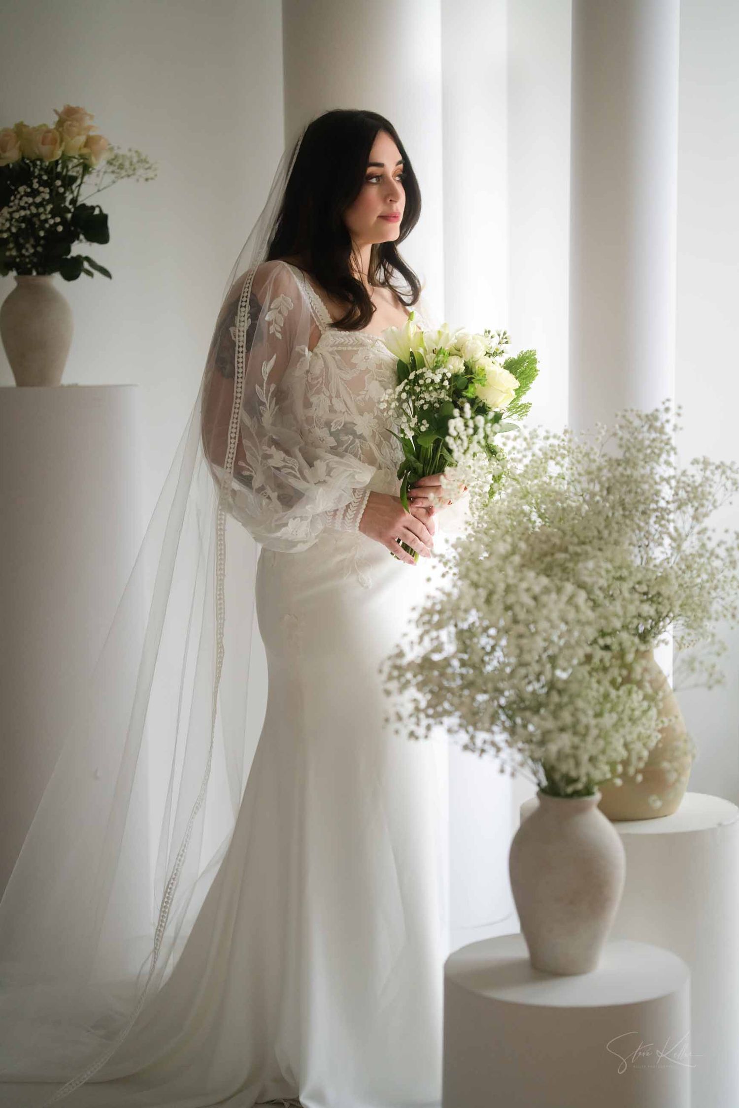 A soft ethereal bridal portrait series featuring white flowers and flowing fabric in a minimalist light-filled setting.