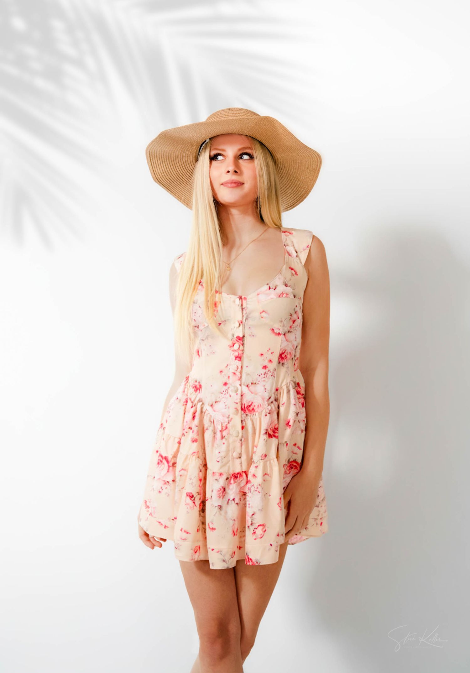 Feminine summer fashion featuring a flowy floral romper in peach tones paired with an oversized straw sun hat.