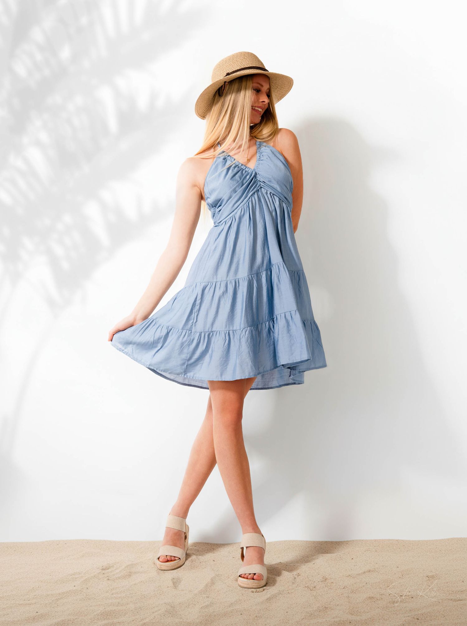 Woman in flowy light blue summer dress and straw hat poses in multiple shots against white background.