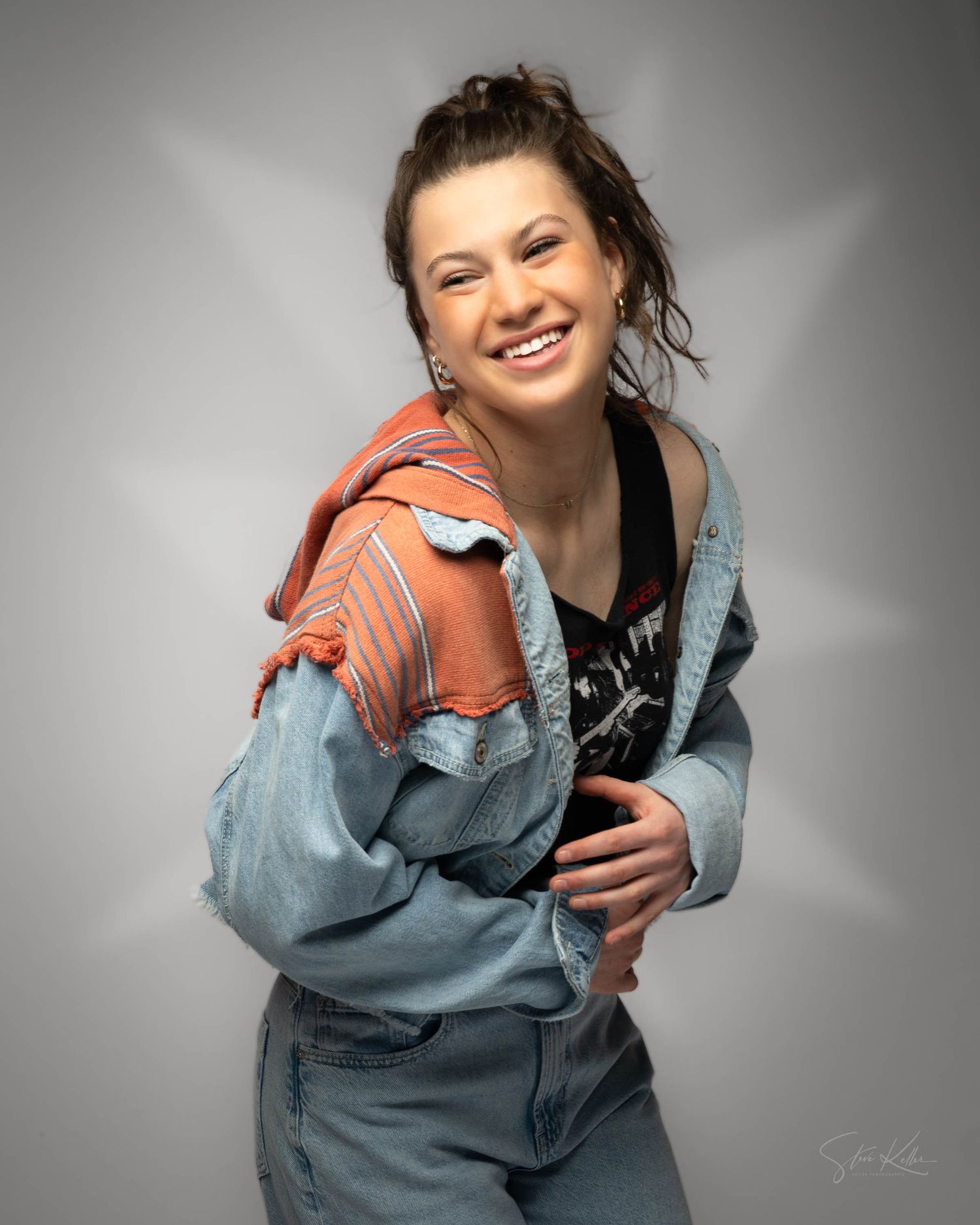 A perfashion modelson wearing denim and a black top poses casually against a gray background in a fun, casual portrait.
