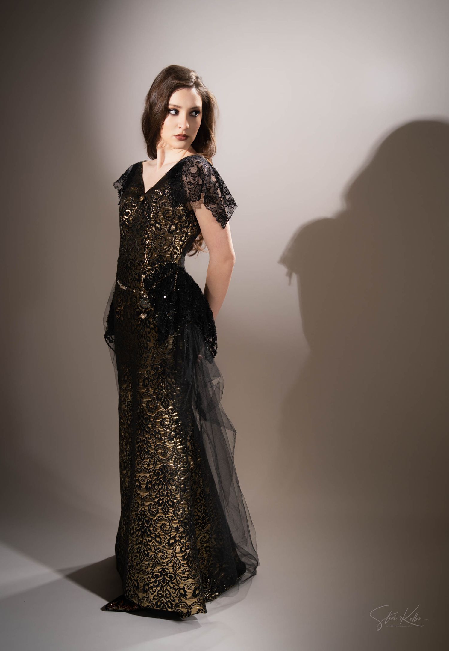 A dramatic fashion photo features a black and gold embellished gown with sheer overlay against a shadowed wall.