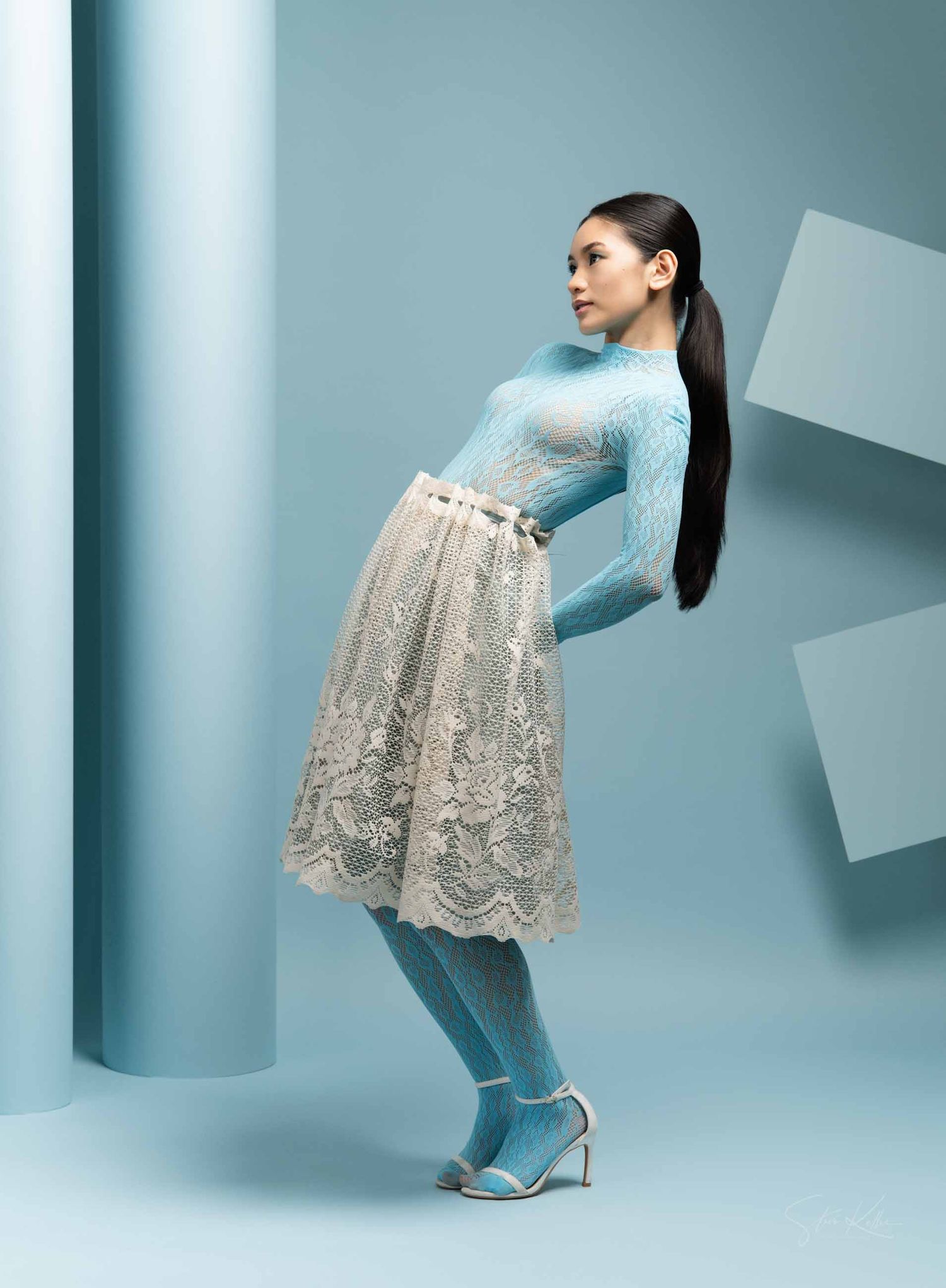 Model in blue denim and lace overlay dress poses against light blue studio backdrop showing different angles.