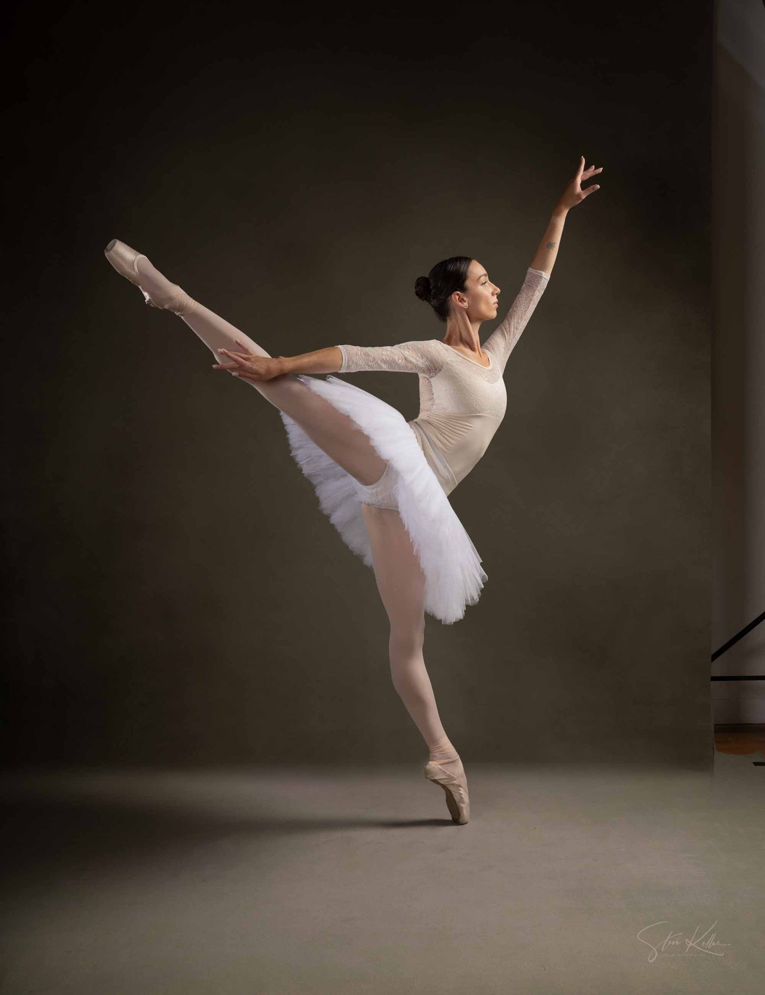 A ballet dancer in a white tutu performs graceful poses and movements against a dark studio backdrop.