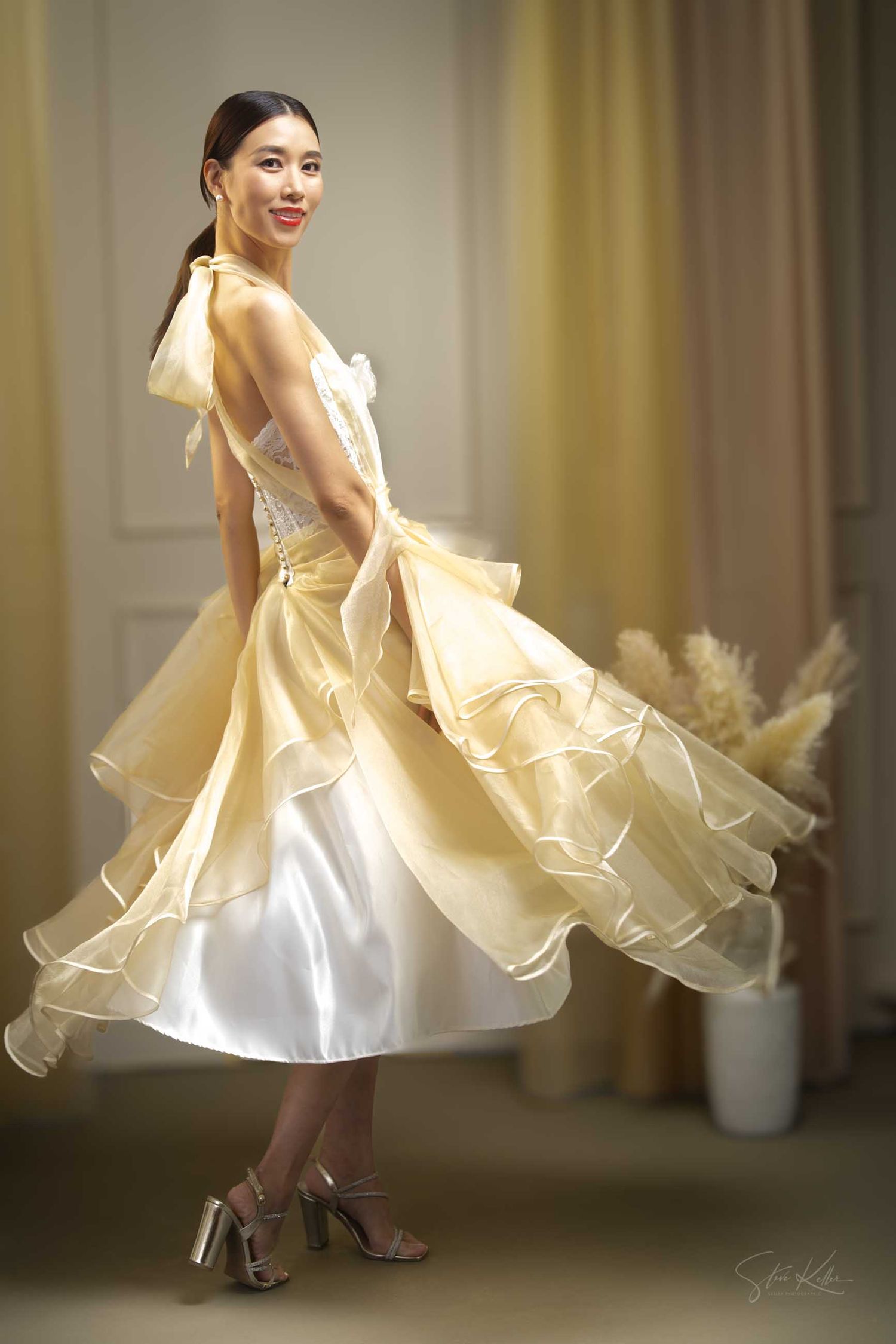 Model twirls in an elegant white and gold party dress with flowing layers.