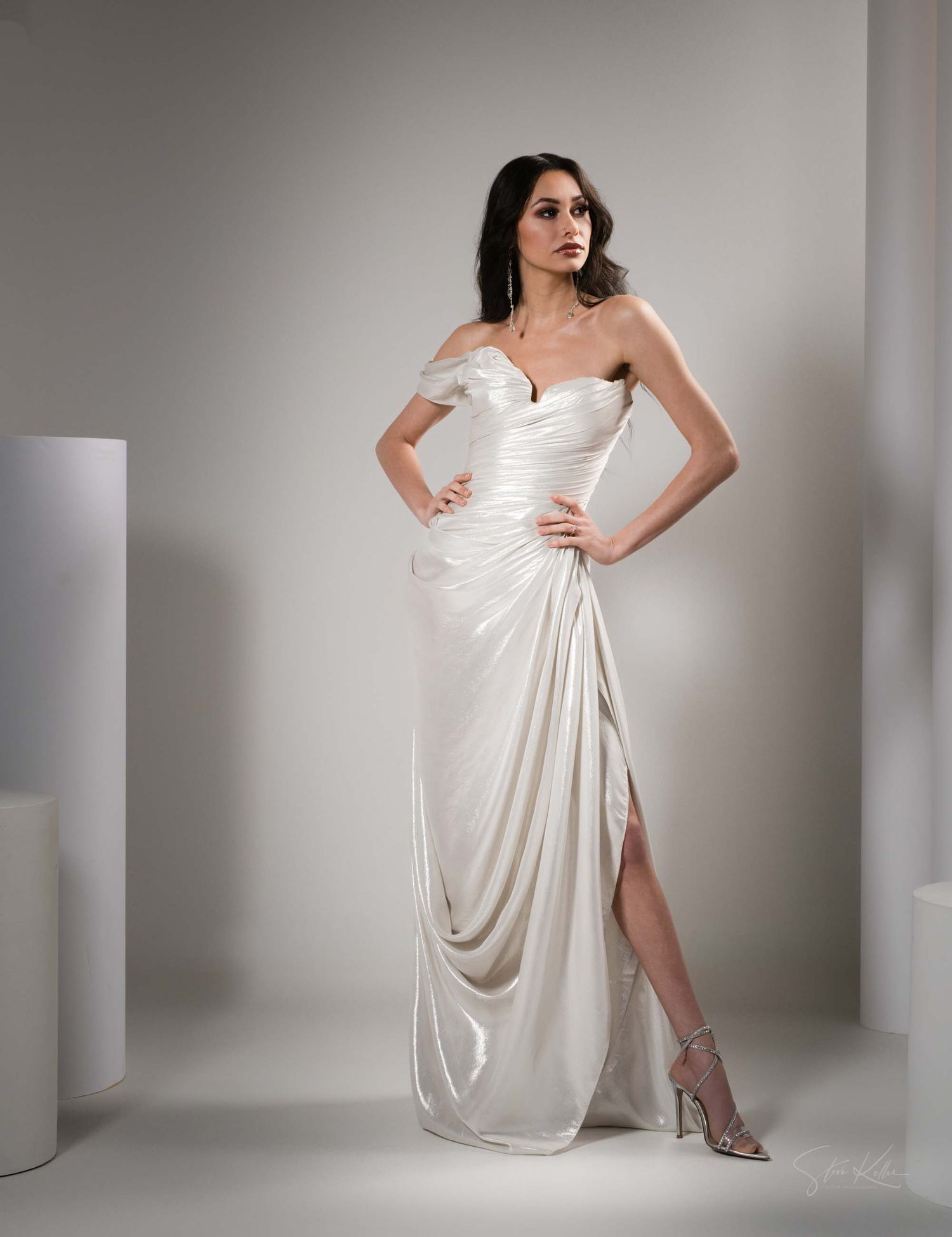 Model in flowing white evening gown poses elegantly against gray studio backdrop showing different angles of the dress.