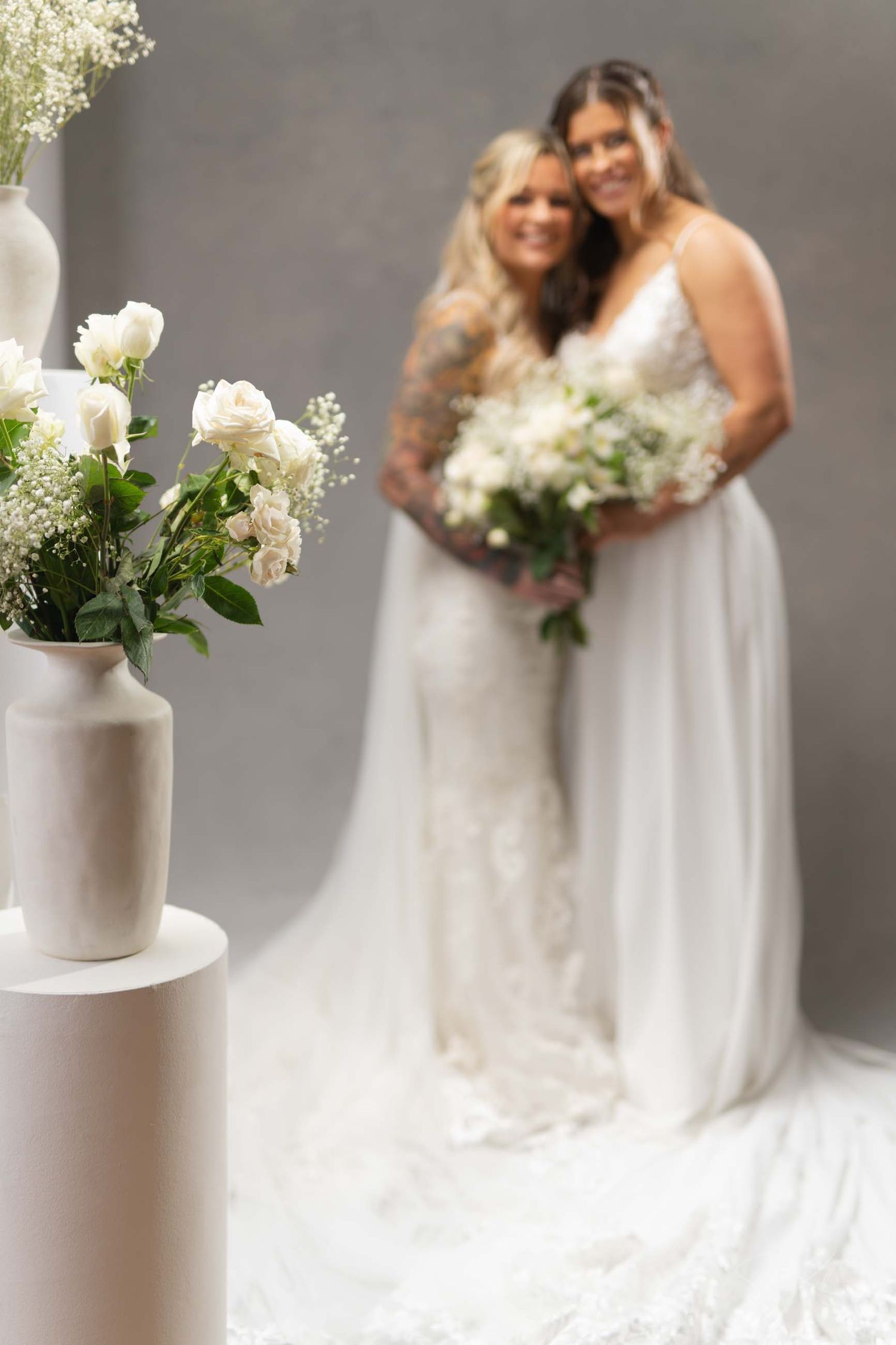 Elegant white floral arrangements in minimalist ceramic vases complement a flowing white wedding dress in a studio setting.