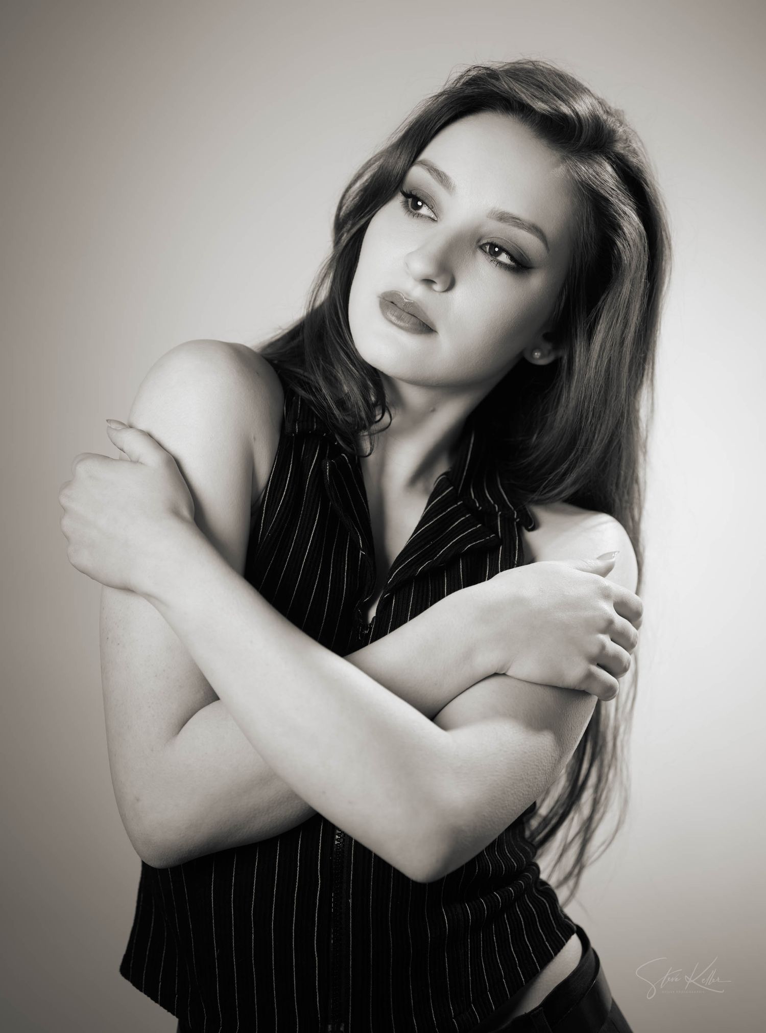 Black and white portrait of person in pinstripe top posing with arms crossed against shoulders in sensual pose.