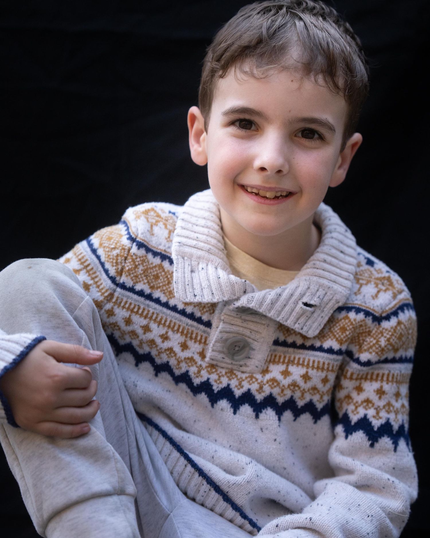 A child in a Fair Isle pattern sweater poses casually against a dark backdrop.