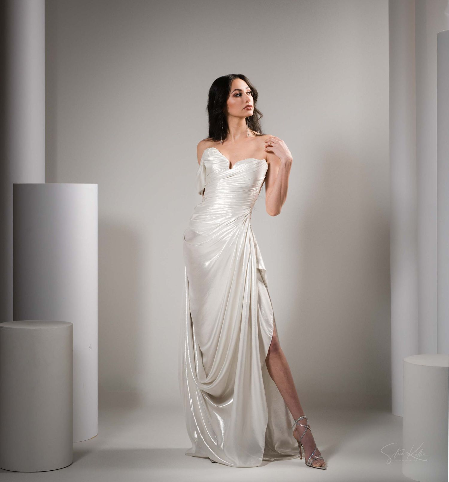 Fashion photoshoot featuring flowing white draped fabric in a minimalist studio setting with soft lighting.