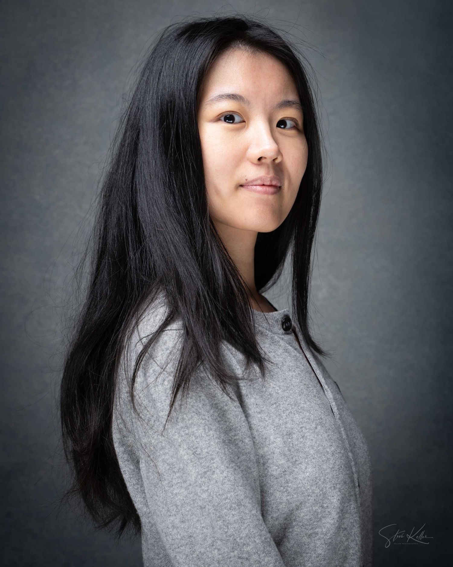 Young Asian woman with long black hair wearing a gray sweatshirt poses for a professional portrait photo.