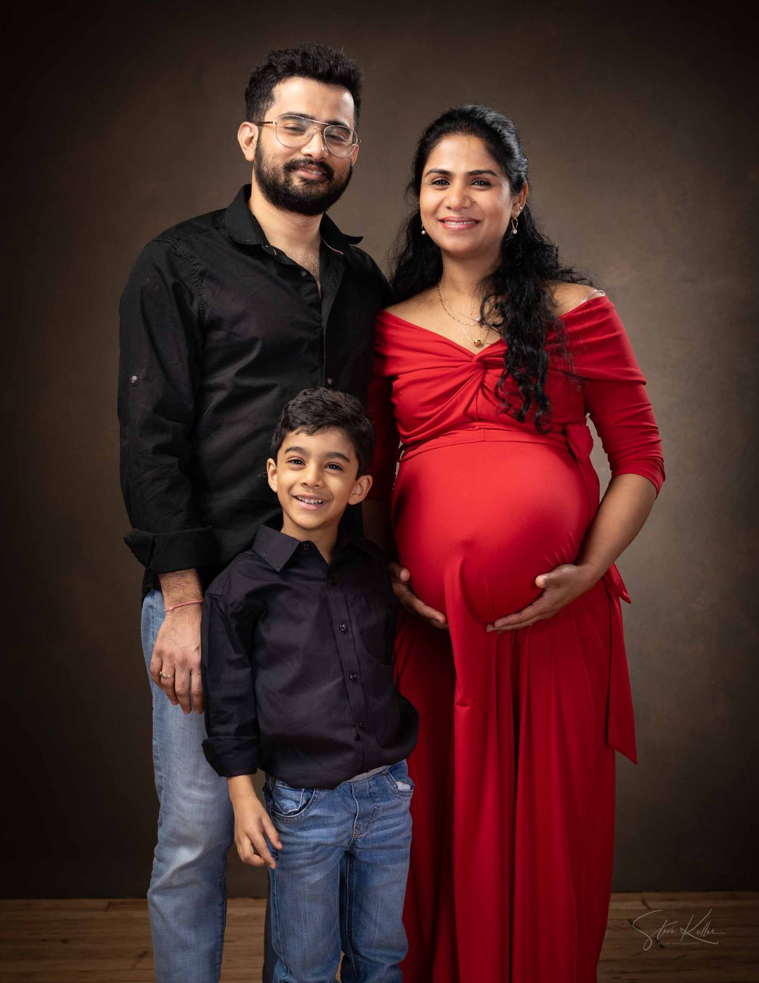 A maternity photo series showing a couple in black and red outfits with their young son against a dark background.