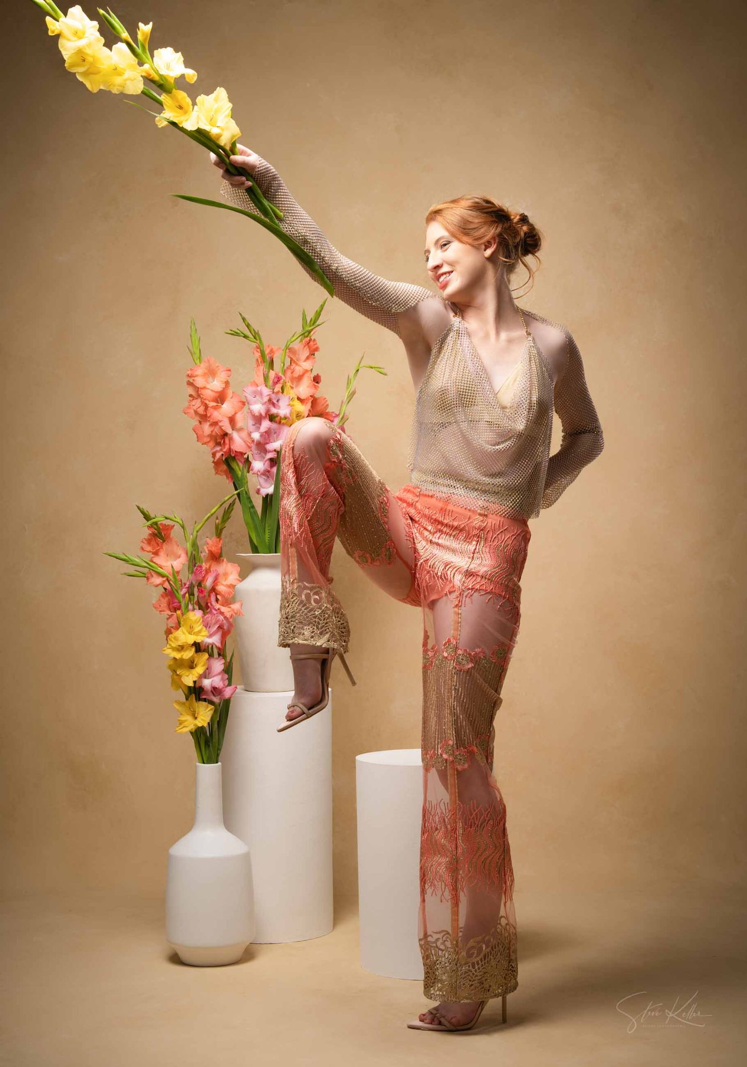 Artistic portrait with gladiolus flowers in white vases and a dancer in coral lace pants striking a graceful pose.