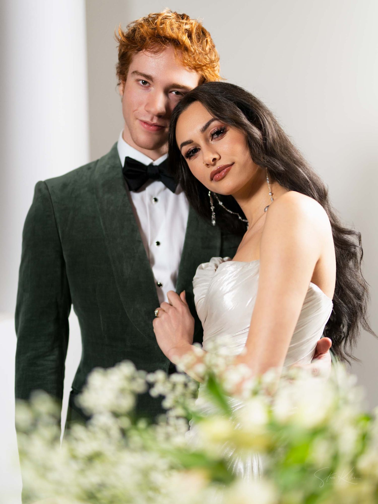 A romantic wedding photo series showing a couple in formal attire posing intimately among white flowers.