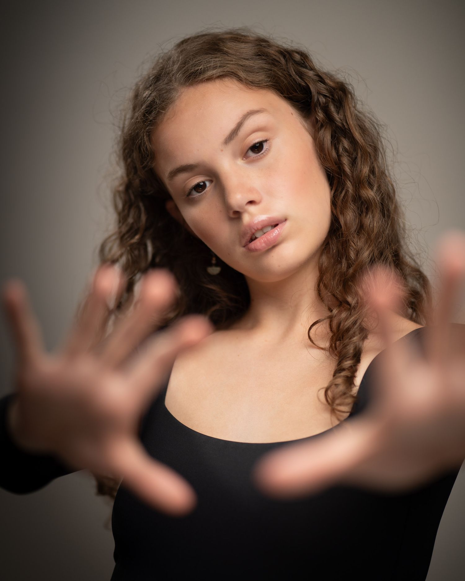 Professional portrait with dramatic hands raised pose against dark background showing beautiful curly hair styling.