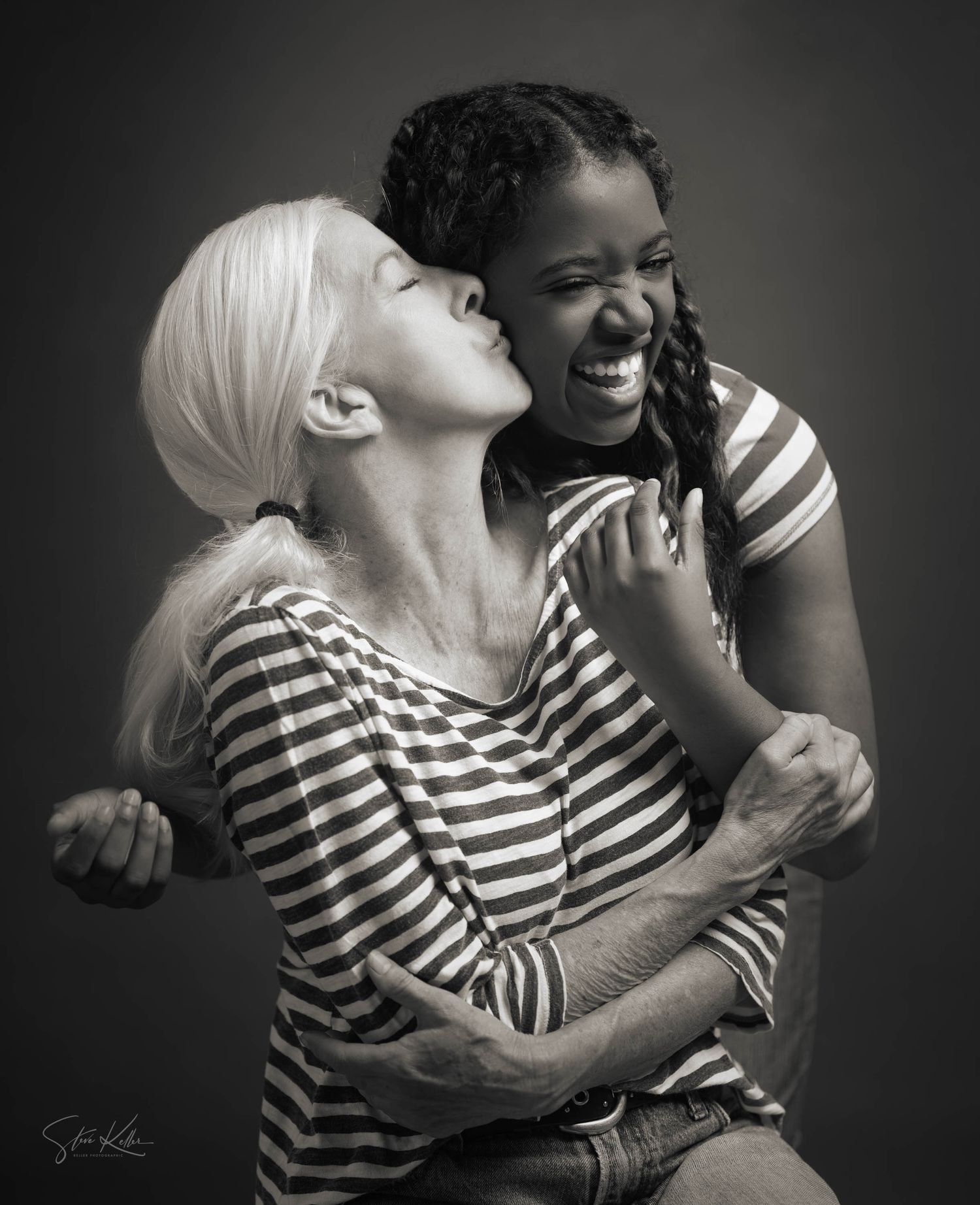 Black and white portrait capturing genuine laughter between two friends in striped shirts.