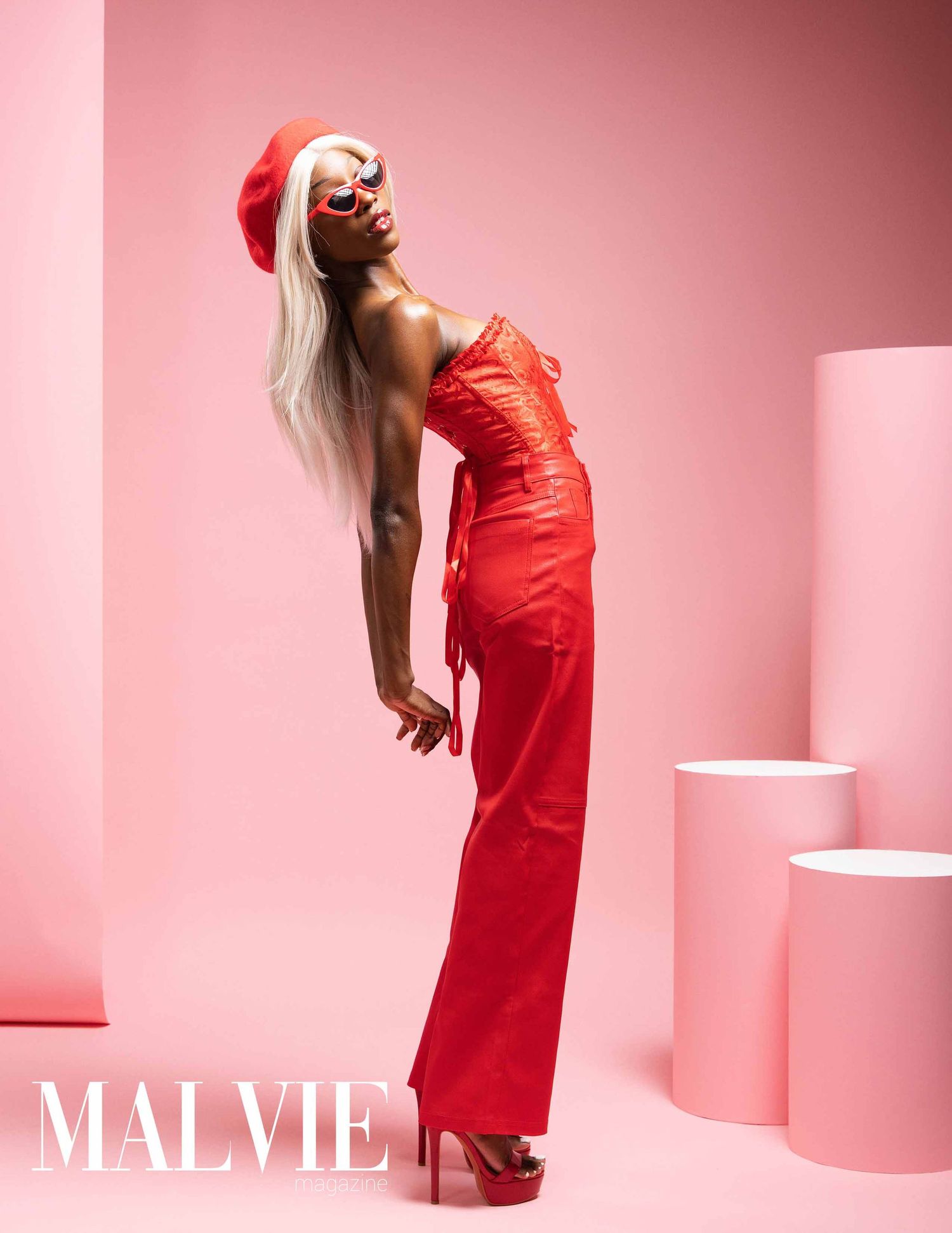 Fashion model in red dress poses dramatically against pink backdrop in artistic studio photoshoot series.
