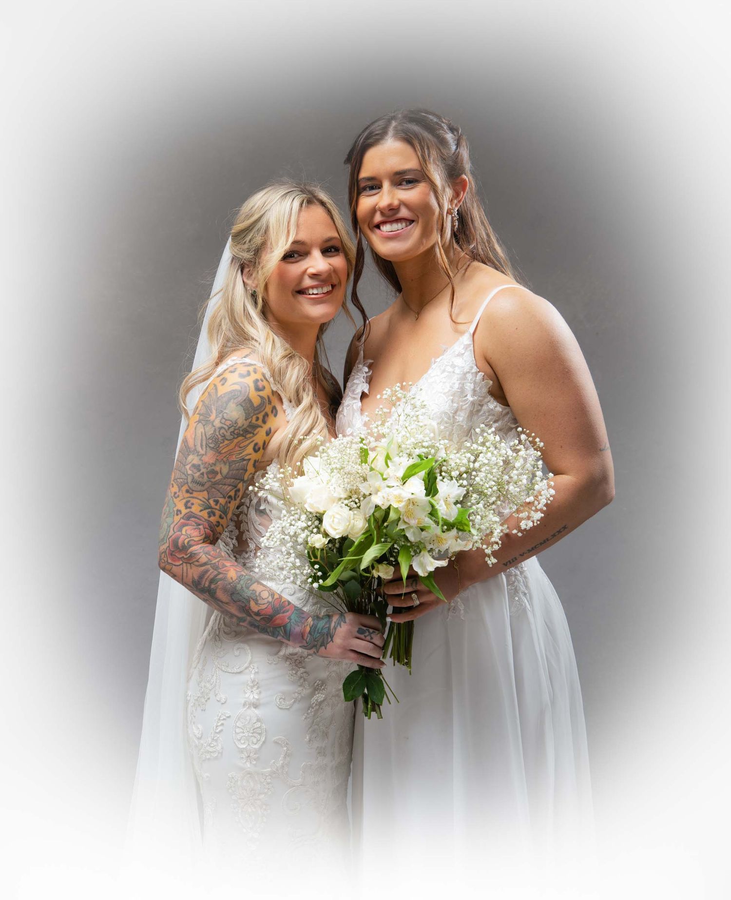 Two brides share joyful moments in white wedding dresses while holding elegant bouquets of white flowers.
