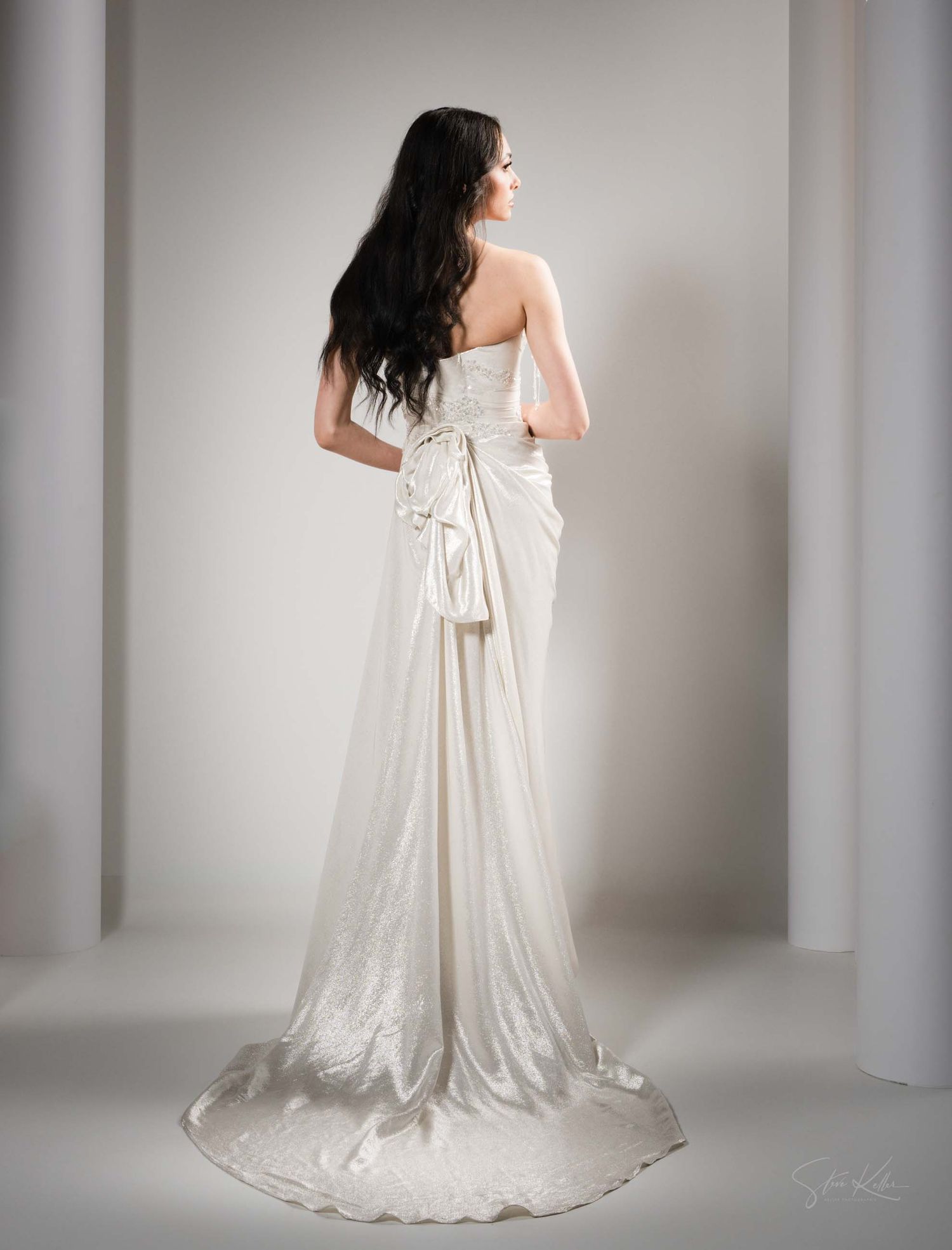 Flowing white wedding dress with train captured in elegant studio portraits against neutral background.