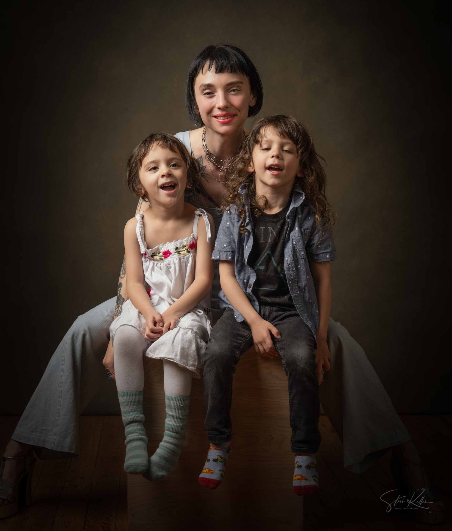 Two children sit together on a dark background, laughing and sharing a playful moment.