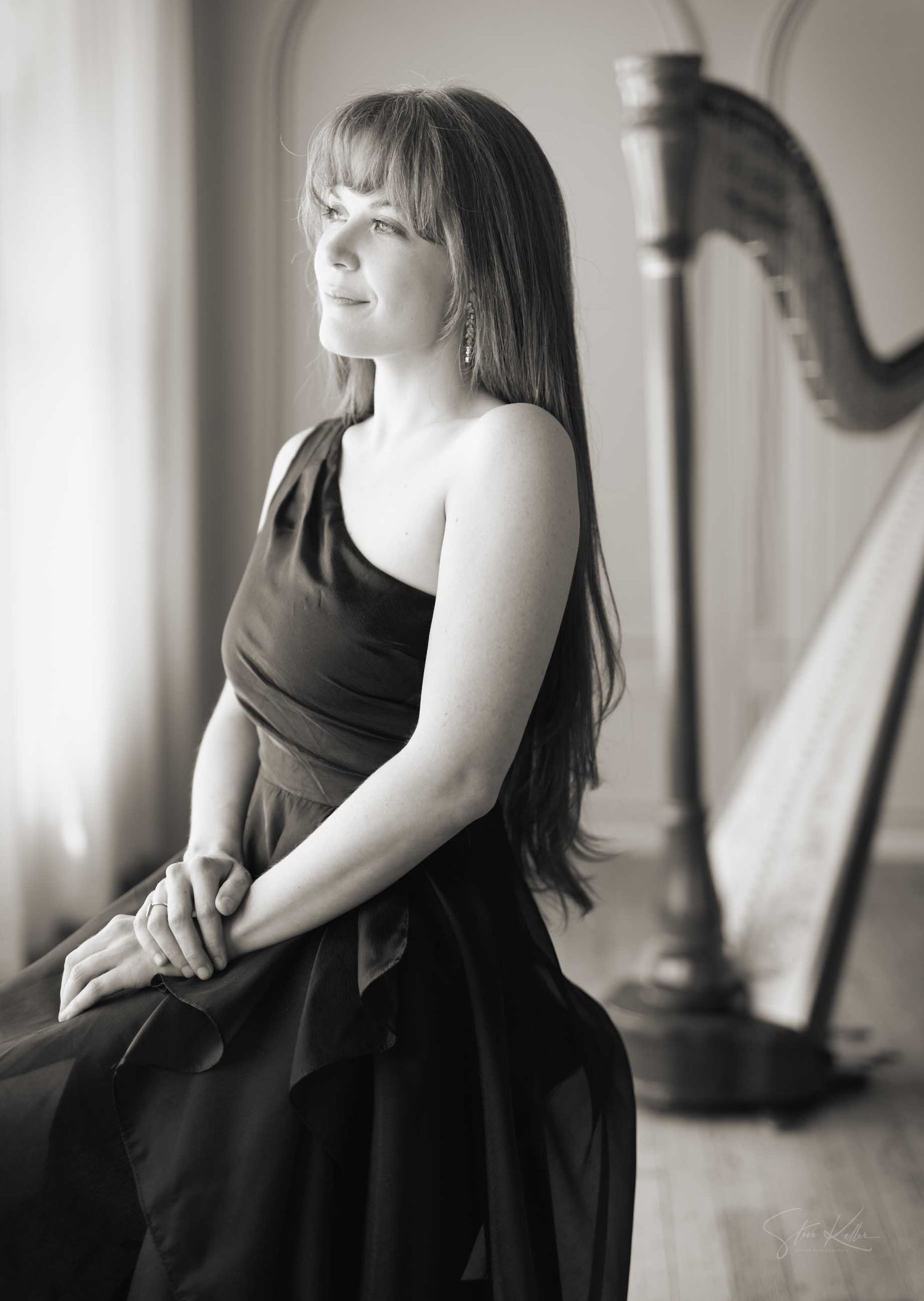 Black and white portrait of a woman in elegant dress seated near a harp, exuding grace and musical artistry.