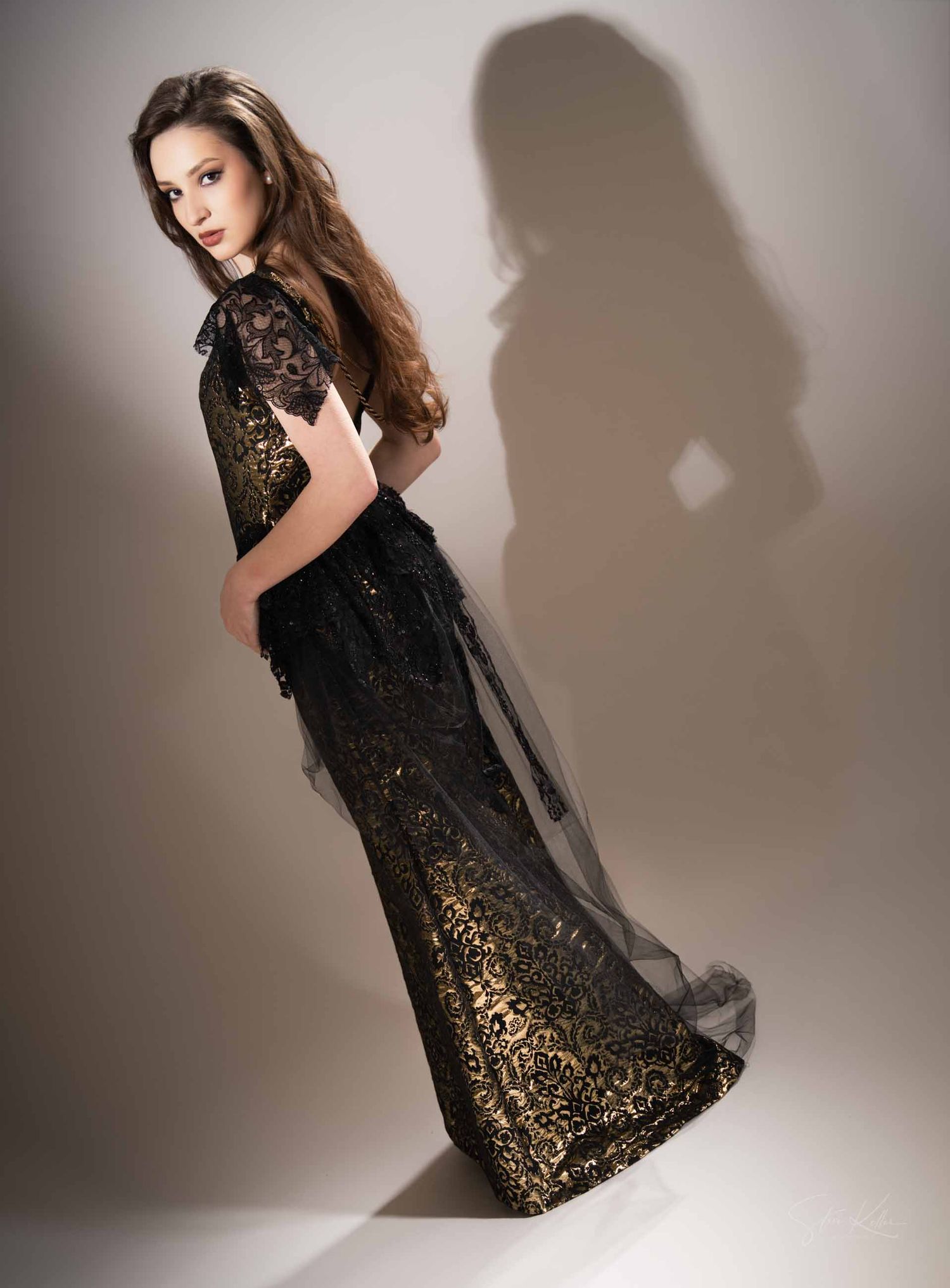 Model in black lace and sequin cocktail dress poses elegantly against neutral studio backdrop.