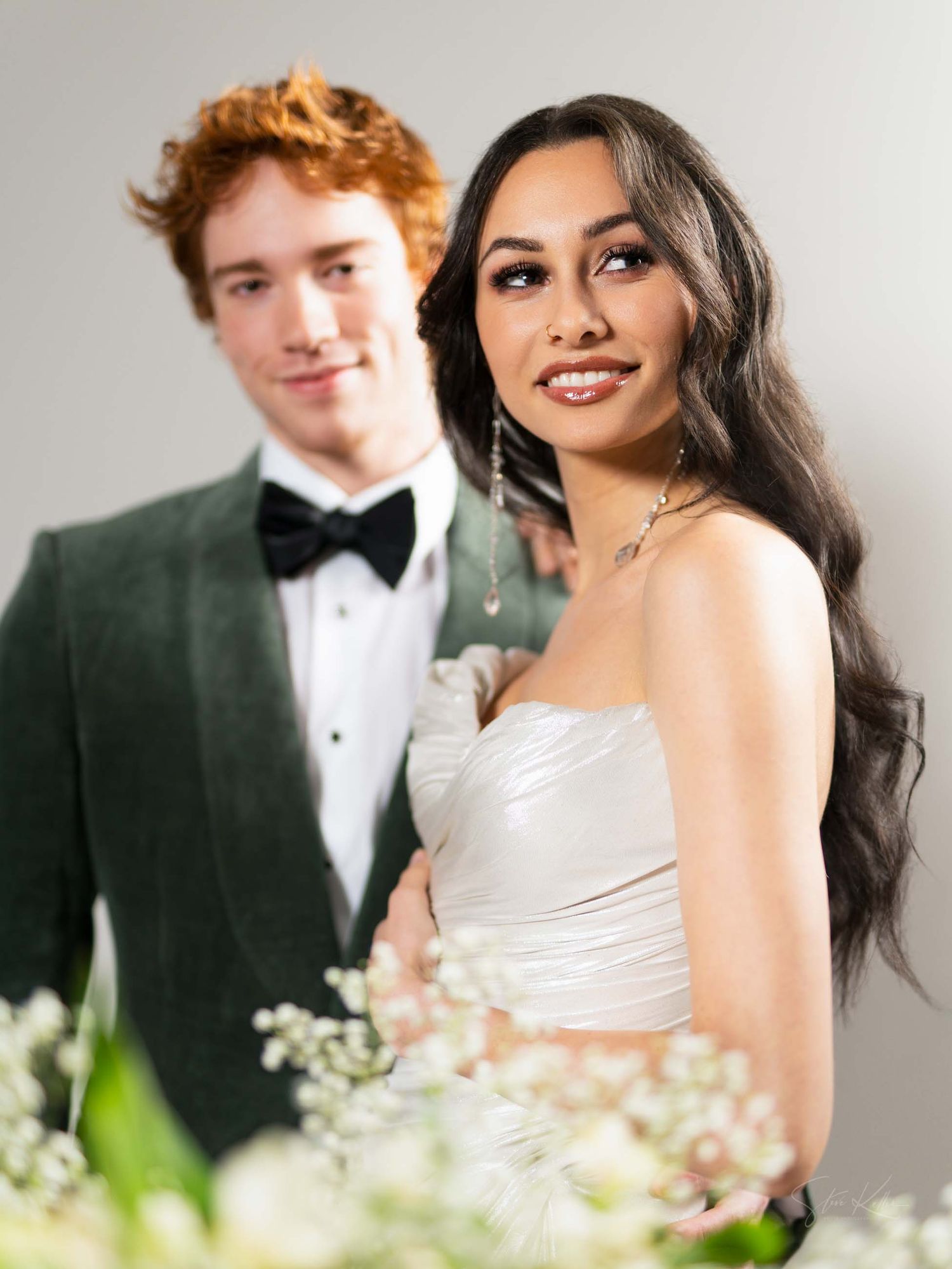 Romantic wedding portrait featuring couple in black tuxedo and white dress with delicate flowers.