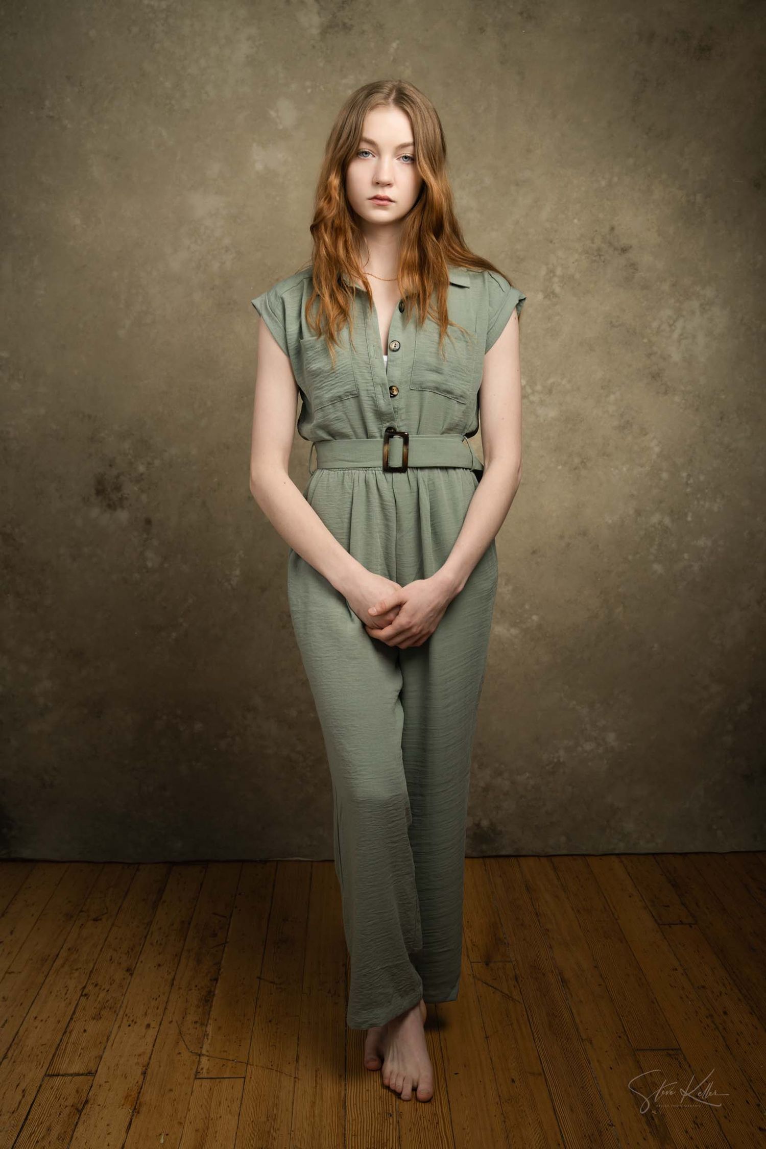 Studio fashion series displaying a sage green sleeveless jumpsuit on wooden flooring.