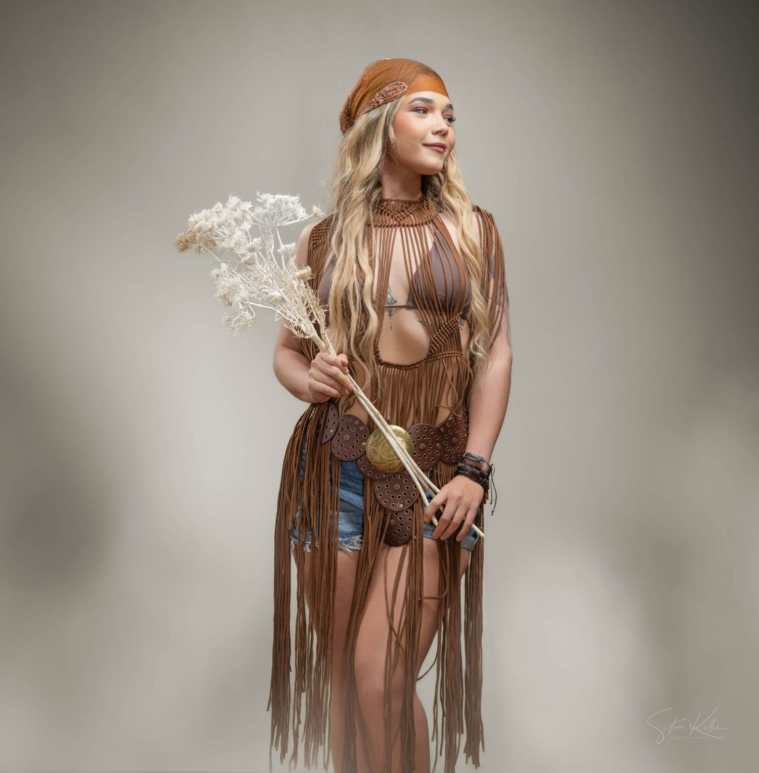 Boho style portrait with orange beret, fringe vest and dried flowers against neutral background.