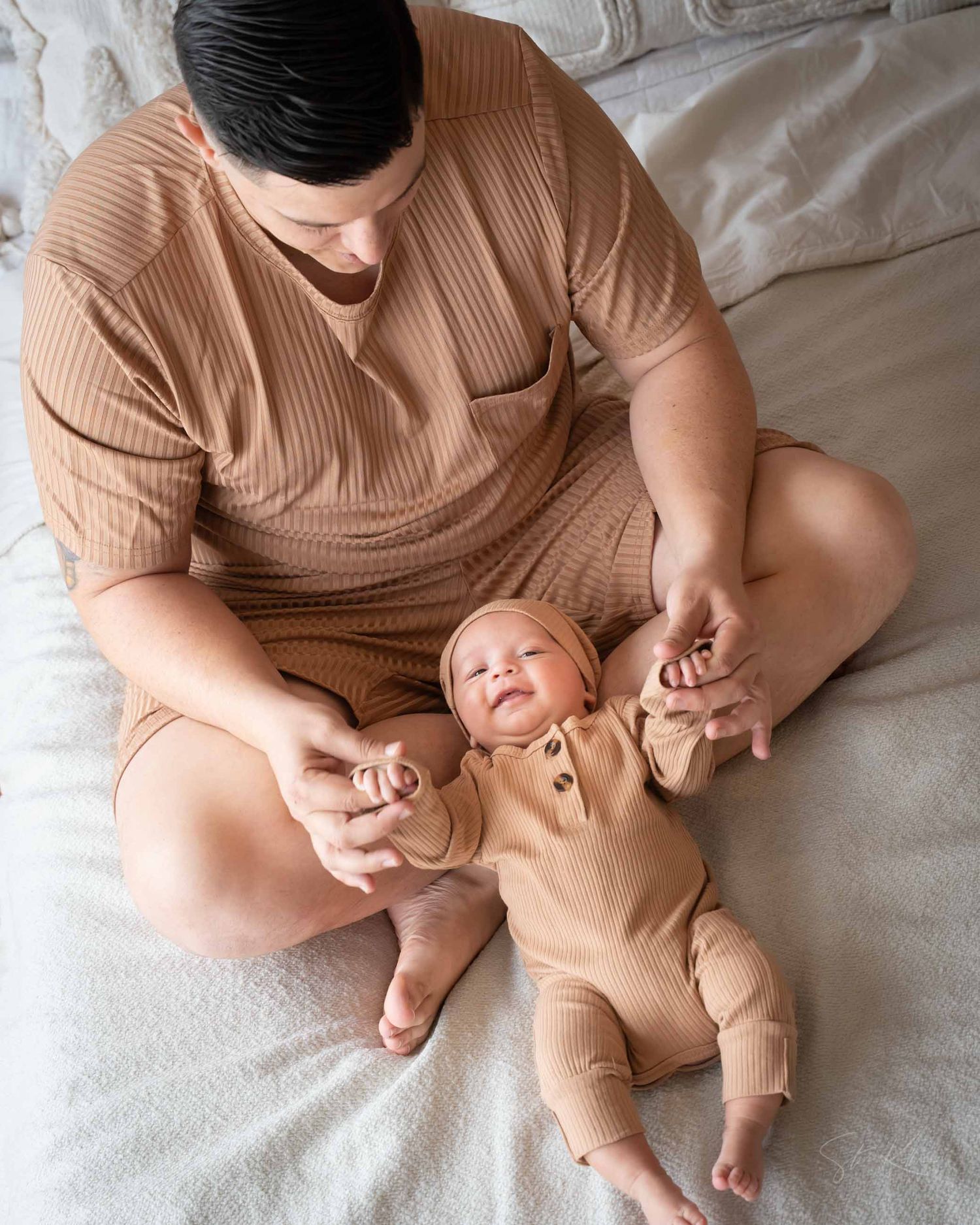 A parent and baby in matching beige outfits lying together on white bedding in a progression of tender moments.