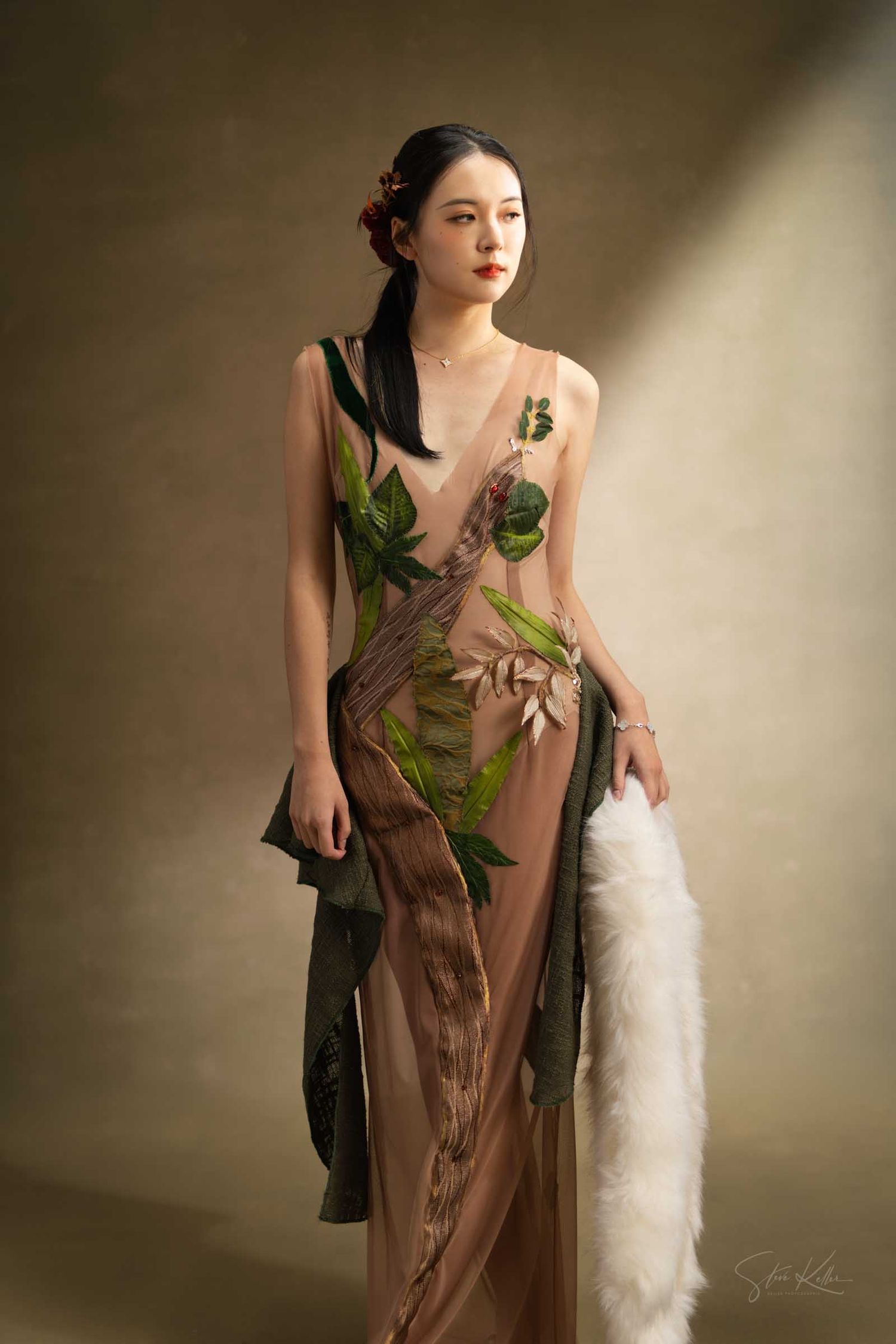 A model in a brown dress adorned with green leaves poses elegantly against a neutral backdrop in a creative photoshoot series.