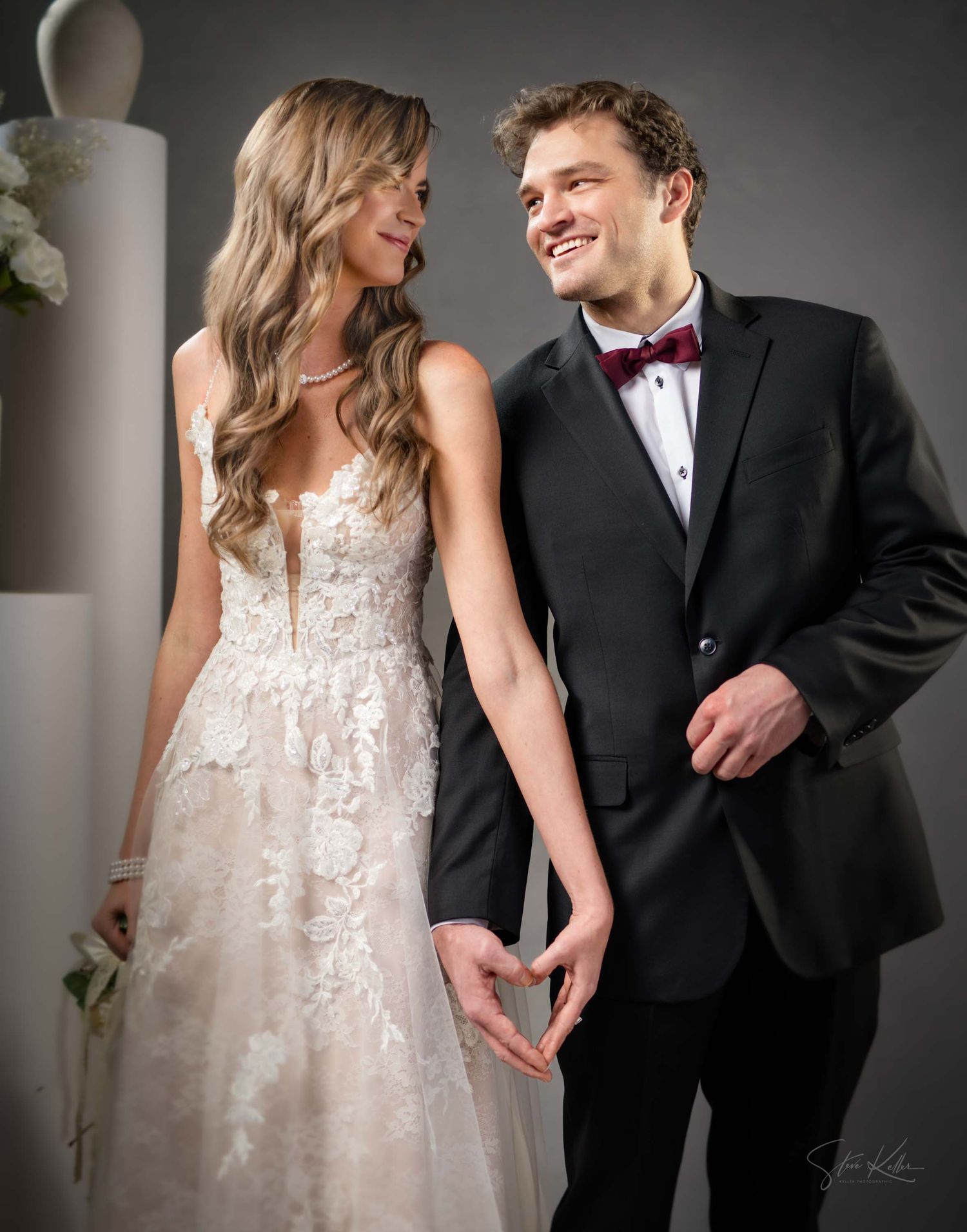 A couple in formal wedding attire share a joyful moment together, with the bride in a lace gown and groom in black tuxedo.
