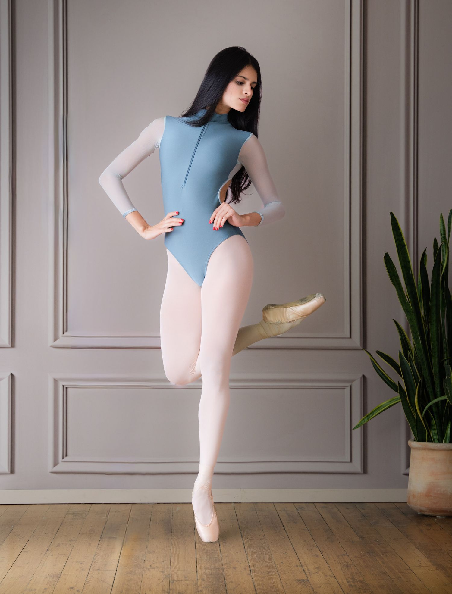 Ballet dancer in blue leotard performs elegant kicks and poses against classic wall paneling.