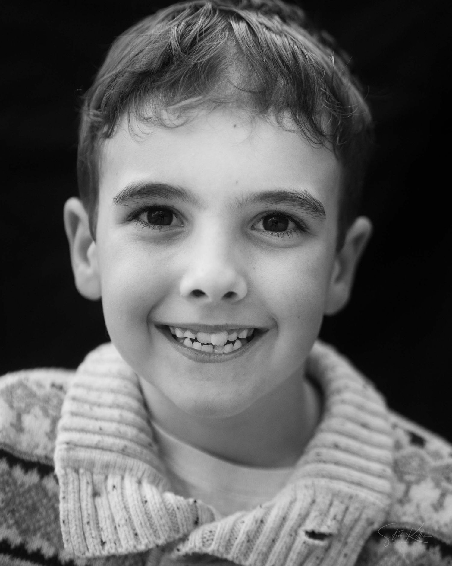 A black and white sequence showing a child's smiling face in a knit sweater from different angles.