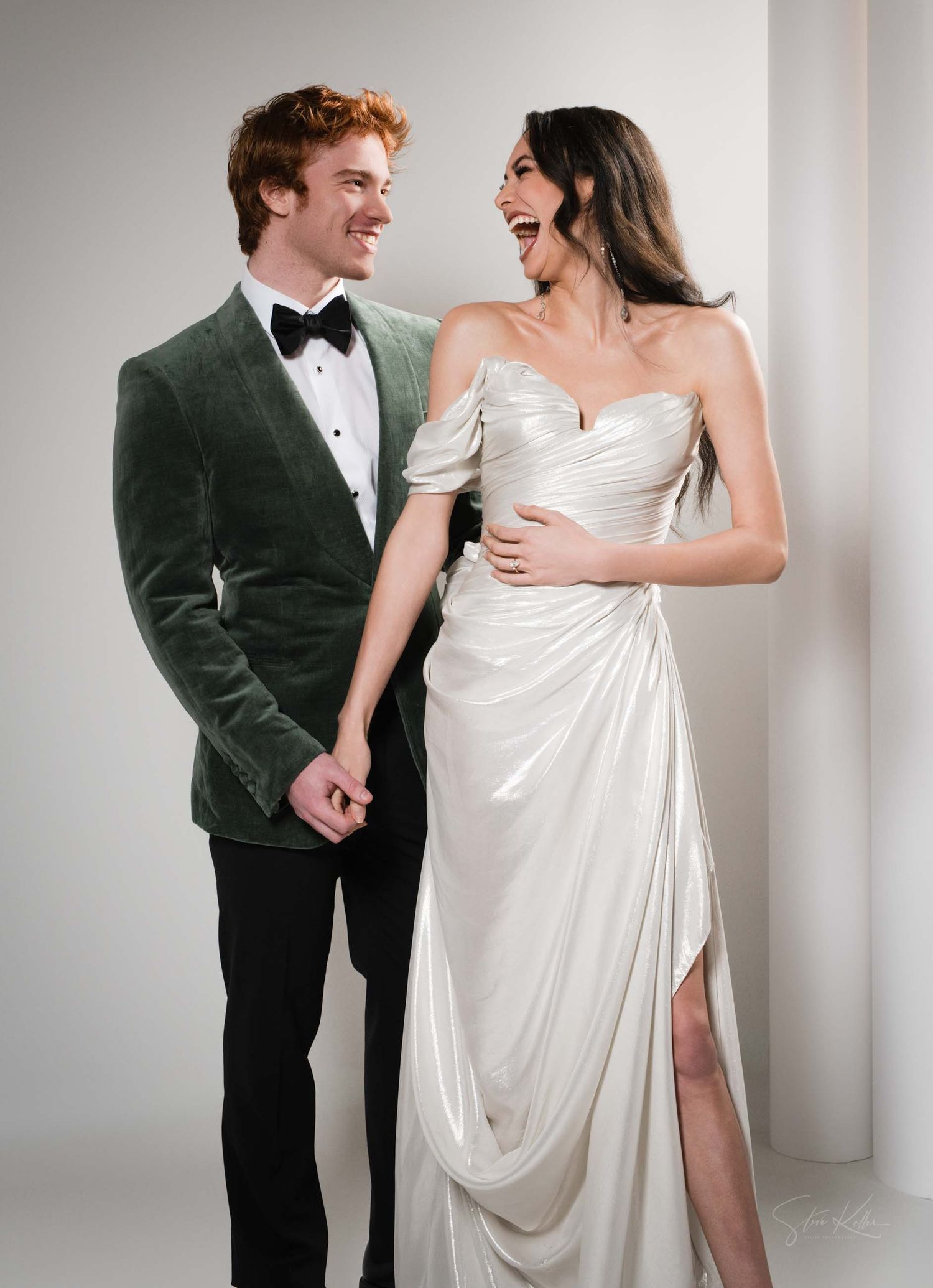 Romantic couple laughing together during wedding photoshoot in studio with bride in white gown and groom in tuxedo.