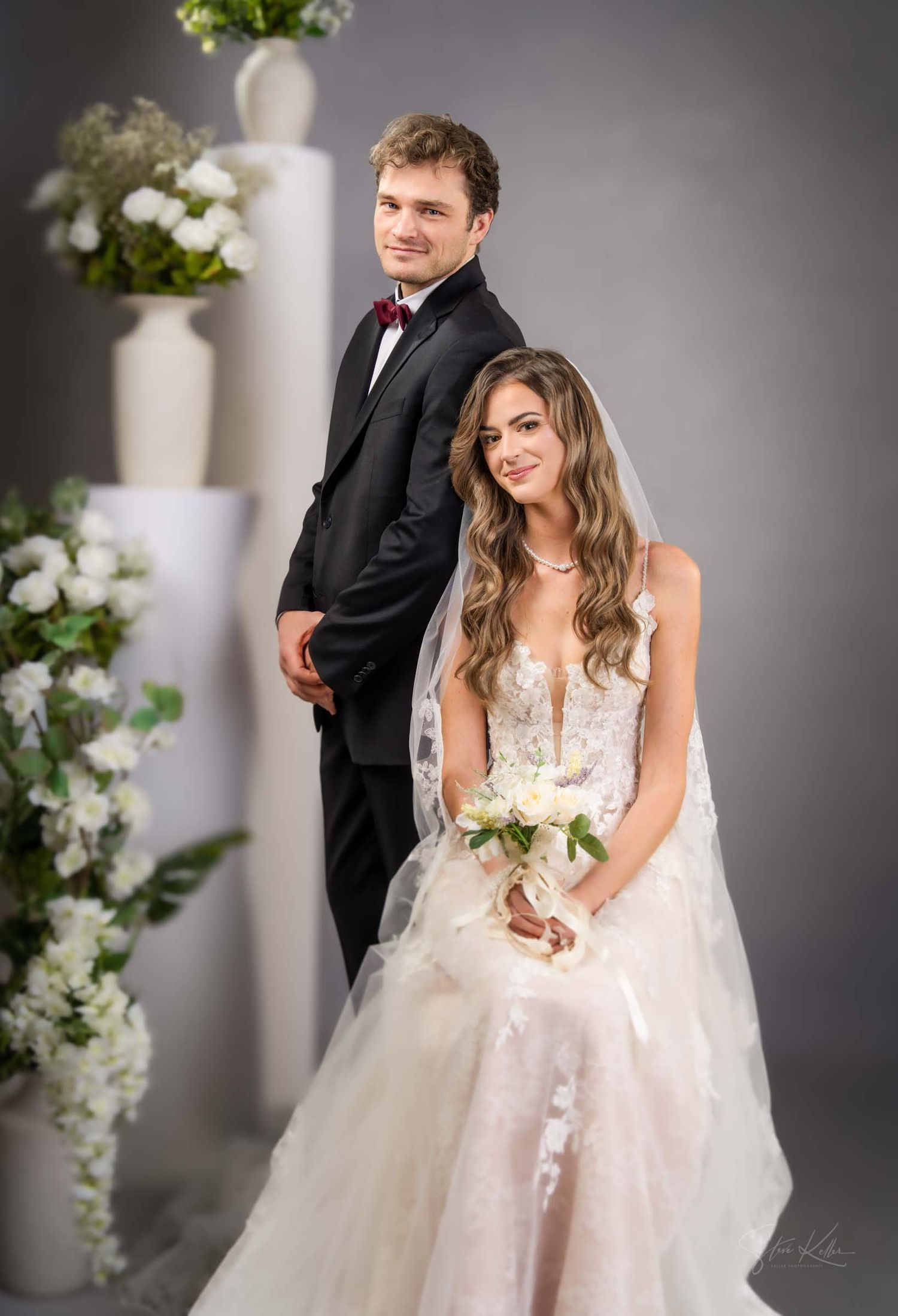 A bride in a flowing white lace gown poses elegantly during a wedding photoshoot with romantic lighting and floral decor.