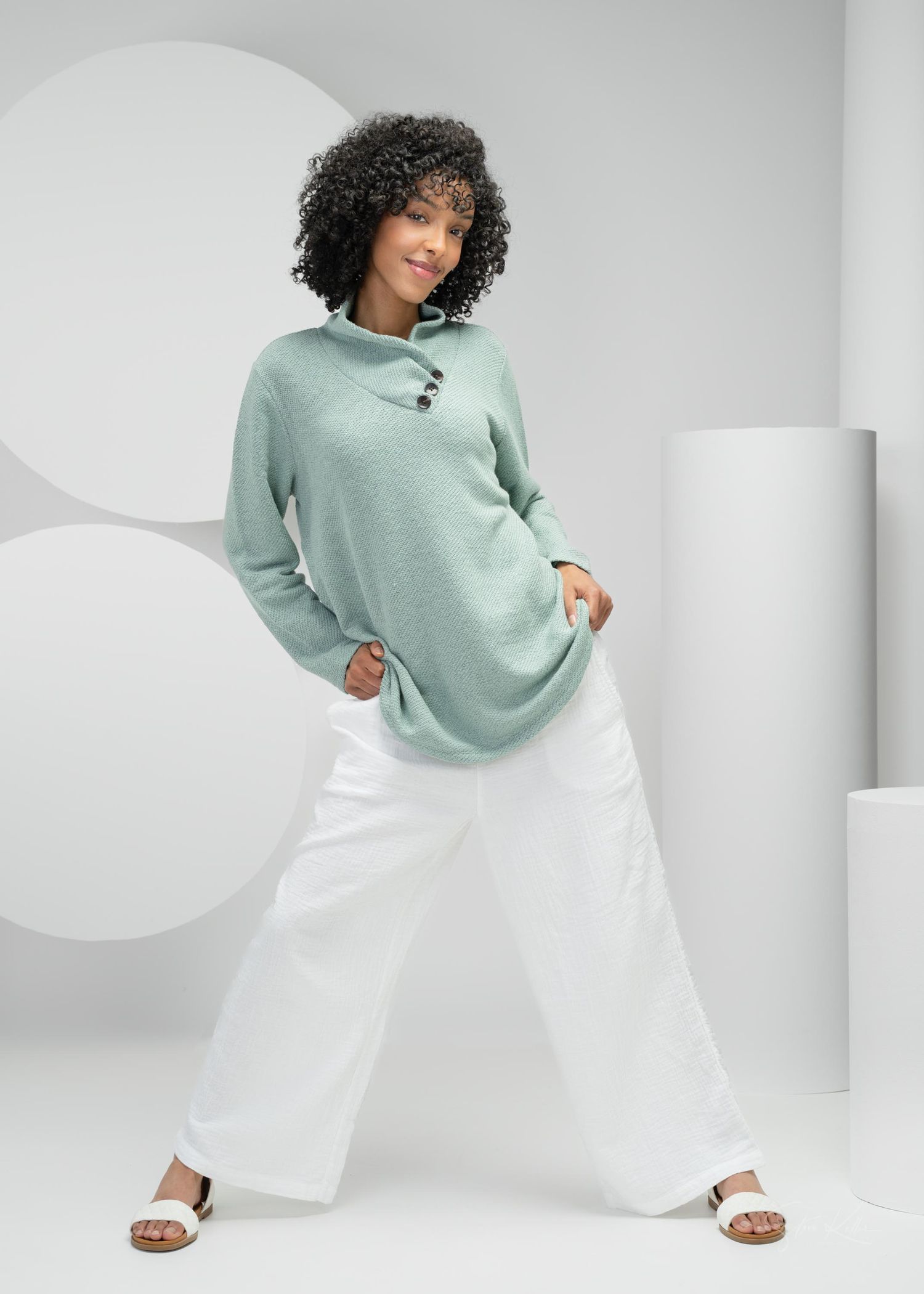 Model wearing mint green oversized sweater with white wide-leg pants and sandals in a minimalist studio setting.