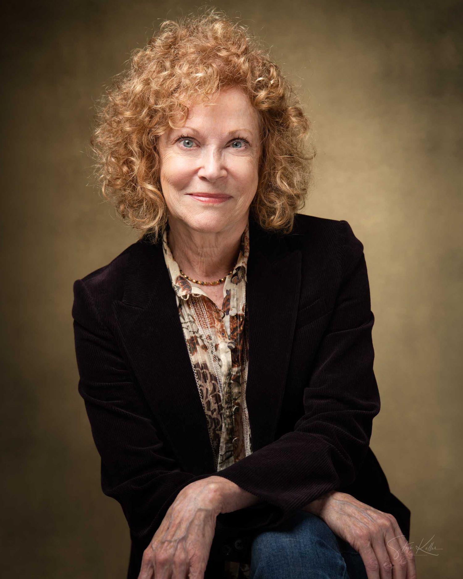 A woman with curly red hair wearing a black blazer poses confidently for a professional portrait photo.